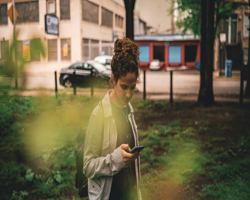 Young adult holding a smartphone in an urban environment with balanced screen brightness